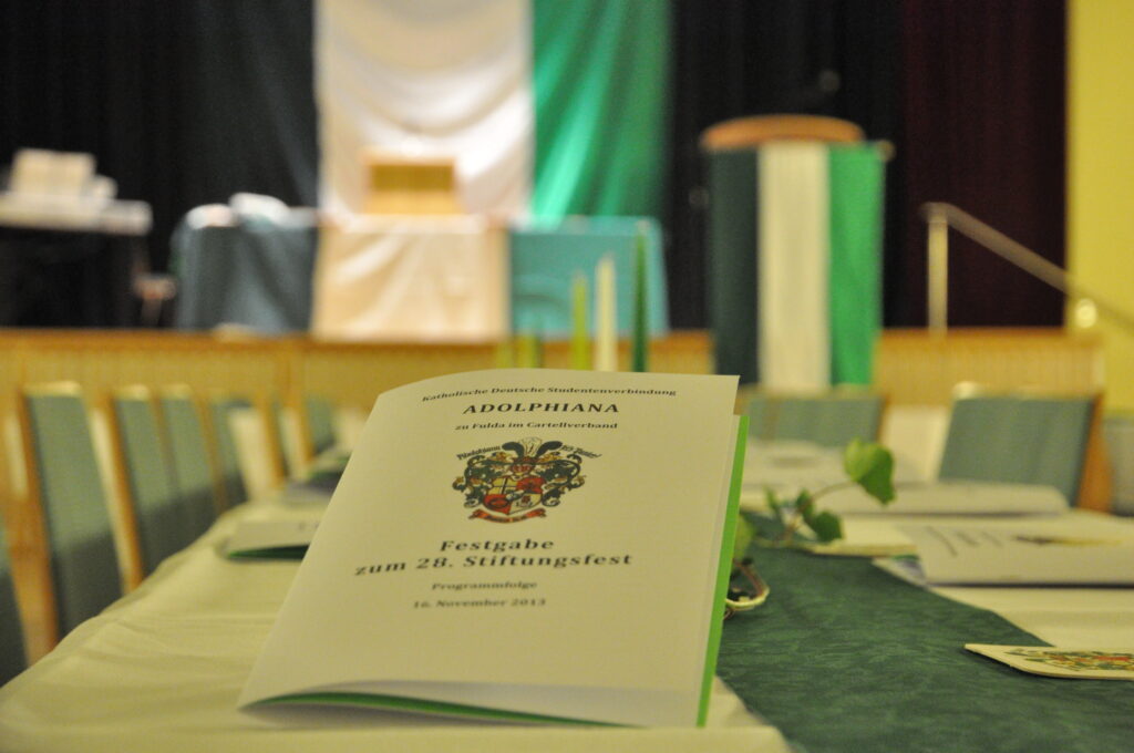 Festschrift auf dem Tisch platziert und im Hintergrund grün-weiß-grüne Fahnen.